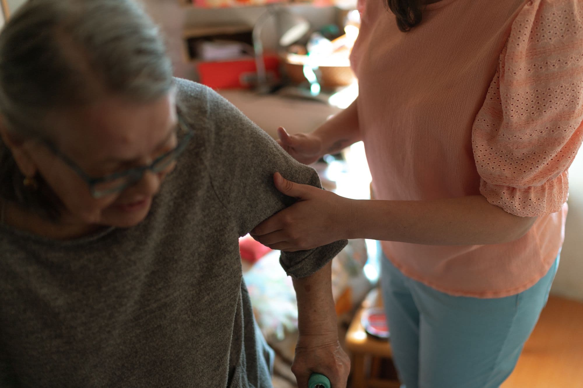 A caregiver helping an older adult adjust a warm layer at home
